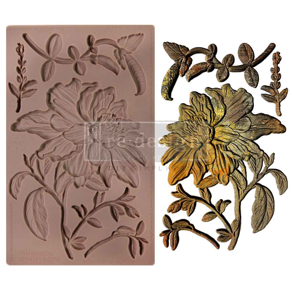 A product image displays a silicone décor mould alongside its finished cast design. On the left is a flexible brown silicone mould containing botanical elements: a large layered flower with detailed petals and leaves, curved stems, small leafy branches, seed pods, and delicate foliage accents. On the right are metallic-finished castings made from the mould, shown in antique gold and bronze tones. The central flower is large and dimensional with flowing petals and realistic veining, surrounded by graceful bo