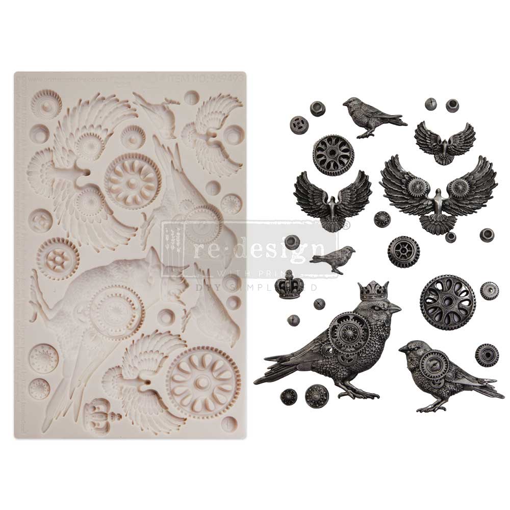 Product display showing a large silicone mould filled with steampunk-inspired bird and wing designs alongside finished cast embellishments in dark metallic tones. The cast pieces include detailed birds with gear-like textures, spread wings, crowns, circular mechanical motifs, and small industrial accents, arranged neatly beside the mould on a clean white background.