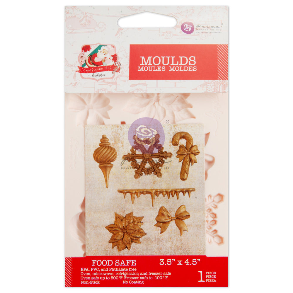 A packaged silicone craft mold is displayed against a white background. The package header is white and red with the word “MOULDS” in large white letters on a red banner, along with a small holiday-themed “Candy Cane Lane” graphic in the top left corner. Through the clear packaging, a cream-colored silicone mold is visible containing holiday shapes including a ribbed ornament finial, a snowflake, a candy cane with a bow, dripping icicles, a poinsettia flower, and a ribbon bow. A sample image on the front sh