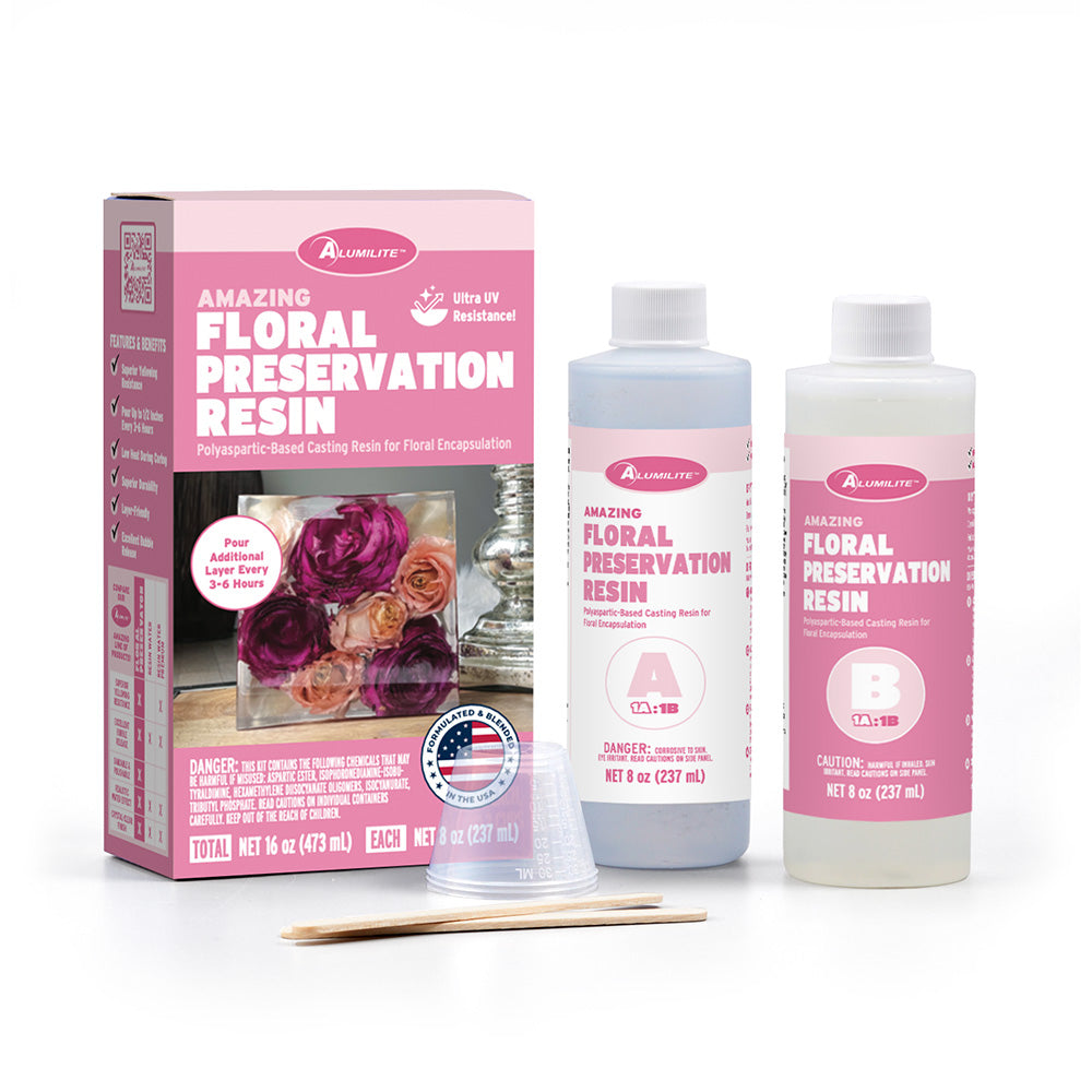 Alumilite Amazing Floral Preservation Resin kit with Part A and Part B bottles, mixing cups, and wooden stir sticks displayed beside pink packaging featuring preserved floral resin artwork on a light gray background.