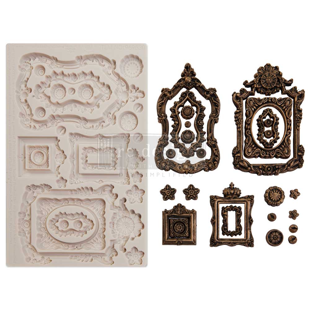 A product-style image showcasing a white silicone décor mold alongside finished ornamental castings in an aged bronze finish. The mold features elaborate vintage-inspired frame designs with scrollwork, floral embellishments, oval and rectangular openings, decorative medallions, and small accent pieces. Arranged beside the mold are completed castings painted in dark metallic bronze with black antiquing, emphasizing the intricate carved details and baroque aesthetic. The clean white background highlights the 