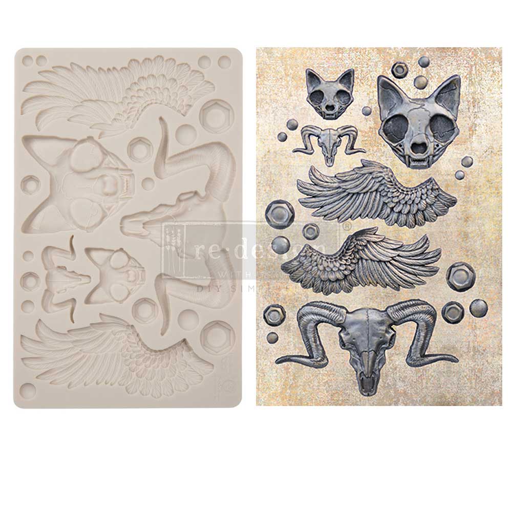 A side-by-side product display shows a cream-colored silicone décor mold on the left and example cast pieces on the right. The mold contains fantasy and Egyptian-inspired elements including feathered wings, ram skulls with curved horns, stylized cat skulls, circular bead accents, and geometric shapes. The finished castings on the right are painted in a dark metallic gray finish with detailed shading that highlights the feathers, horns, and skull textures. The layout presents mirrored wing sets, large and sm